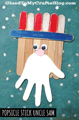 A Popsicle Stick Uncle Sam craft featuring a blue stick for the hat brim, red and white hat, googly eyes, pink nose, and a white paper beard cutout, all set against a starry teal background.