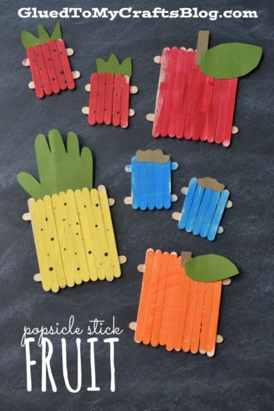 Colorful popsicle stick fruit crafts shaped like a pineapple, apple, watermelon, blueberry, and orange are displayed on a black background with "popsicle stick FRUIT" text.
