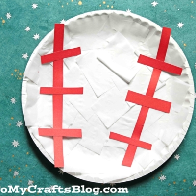 A paper plate baseball craft decorated with red paper strips for stitches, set on a teal, speckled background.