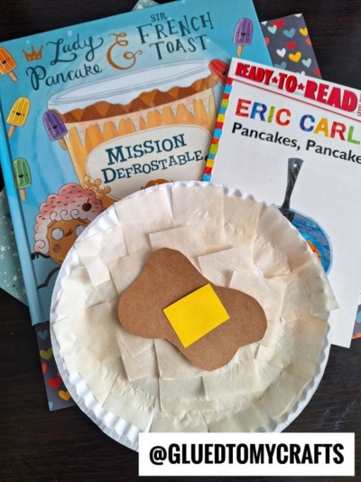 Two children’s books about pancakes and a story time craft—a paper plate pancake with brown paper "syrup" and yellow "butter"—displayed on a table with the handle @GLUEDTOMYCRAFTS. Perfect inspiration for Eric Carle crafts!.