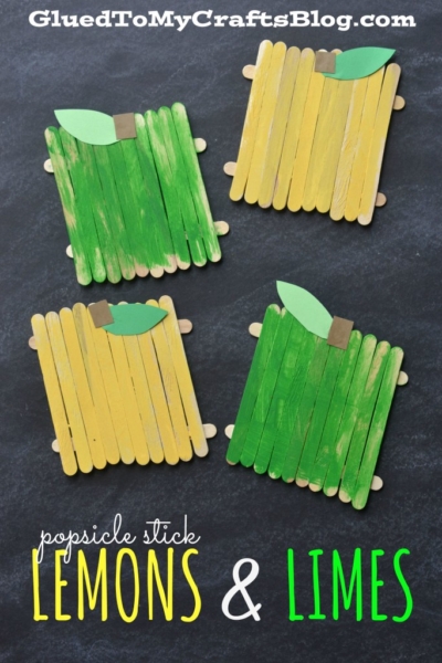 Four square coasters made from yellow and green popsicle sticks, designed to resemble popsicle stick fruit like lemons and limes with paper leaves and brown stems, arranged on a black surface. Text at the top and bottom describes the craft.