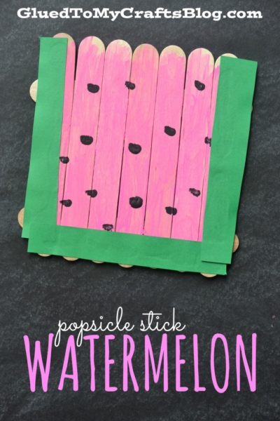 A popsicle stick fruit craft made from sticks painted pink with black dots and bordered with green paper, designed to look like a watermelon slice and labeled popsicle stick WATERMELON.
