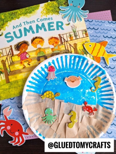 A children’s book titled “And Then Comes Summer” is shown with an under the sea craft: a paper plate ocean decorated with sea creature stickers and brown paper strips, surrounded by more sea-themed paper cutouts.