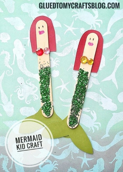 Two craft stick mermaid creations made from popsicle sticks, green glitter, colored gems, and paper tails are displayed on a sea-themed background with the text MERMAID KID CRAFT and GLUEDTOMYCRAFTSBLOG.COM.