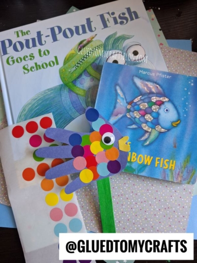 Children's books The Pout-Pout Fish Goes to School and The Rainbow Fish are paired with a colorful, handprint fish craft made of paper and stickers, displayed on patterned paper. Create your own handprint fish puppets for an interactive storytime experience!.