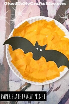 A white paper plate covered with orange tissue squares showcases a black paper bat with white eyes in the center, creating a "paper plate fright night" scene. The image includes “GluedToMyCraftsBlog.com” and the text “Paper Plate Fright Night.”.