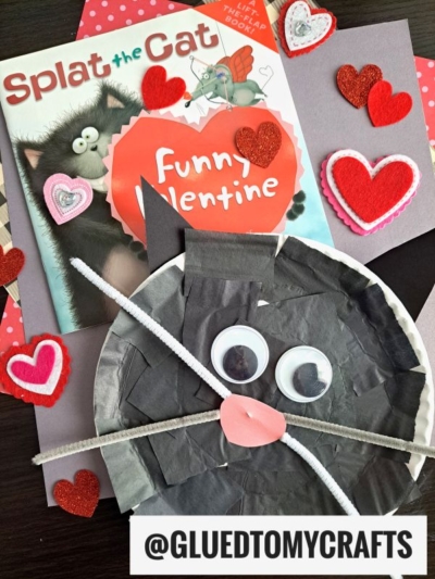A childrens book titled Splat the Cat: Funny Valentine surrounded by handmade Valentines Day cat crafts, felt hearts, a gray paper plate cat with googly eyes, a pink nose, pipe cleaner whiskers, and a cute tissue paper black cat.
