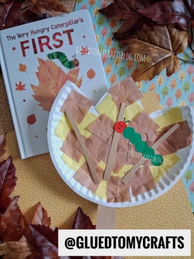 A children’s book titled The Very Hungry Caterpillar’s First with a fall-themed caterpillar craft made from a paper plate and tissue paper, surrounded by colorful paper plate leaf creations and autumn leaves on a polka dot surface.