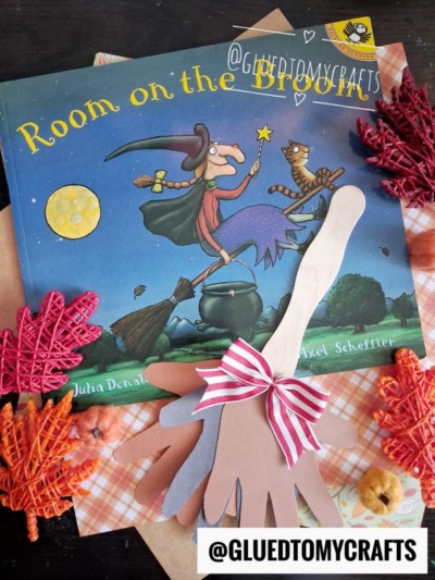 A “Room on the Broom” book is displayed alongside a charming handprint broom craft, complete with a popsicle stick broom, red and orange textured leaves, and a striped bow. The IG handle @GLUEDTOMYCRAFTS appears in two spots.