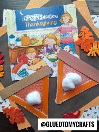 The Night Before Thanksgiving book displayed next to two popsicle stick pumpkin pies made from orange paper and cotton balls, all surrounded by felt leaves.