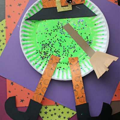 A whimsical melted witch craft features a green-painted paper plate, glitter, a paper hat, pumpkin-patterned legs, black boots, and a broom on colorful paper—perfectly labeled PAPER PLATE MELTED WITCH.