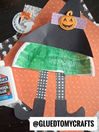 A Halloween witch craft featuring paper plate witch legs, made from colored paper, tissue paper, and a pumpkin sticker, shown with glue and patterned papers. Text says @GLUETOMYCRAFTS.