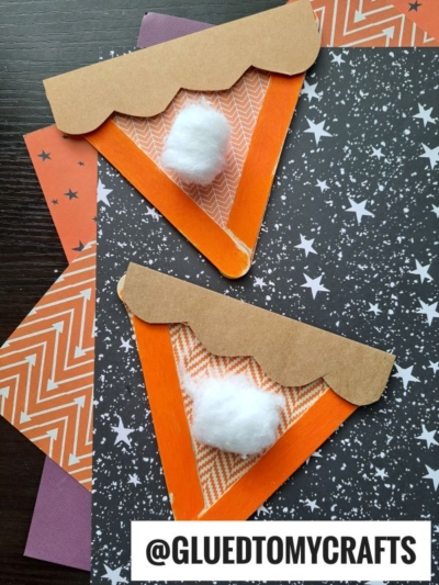 Two paper pumpkin pie slice crafts with orange triangles, brown crusts, and cotton ball toppings—resembling adorable popsicle stick pumpkin pies—are placed on star and zigzag patterned paper backgrounds. @GLUEDTOMYCRAFTS is visible at the bottom.