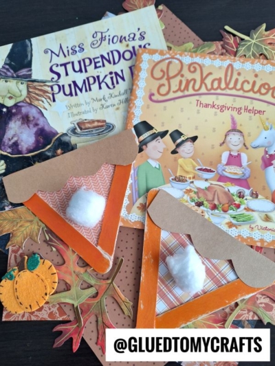 Two children’s Thanksgiving books lie on autumn leaves. In front are craft stick pumpkin pie creations with orange slices, cotton ball “whipped cream,” and brown crusts. A felt pumpkin and @GLUEDTOMYCRAFTS are also visible.