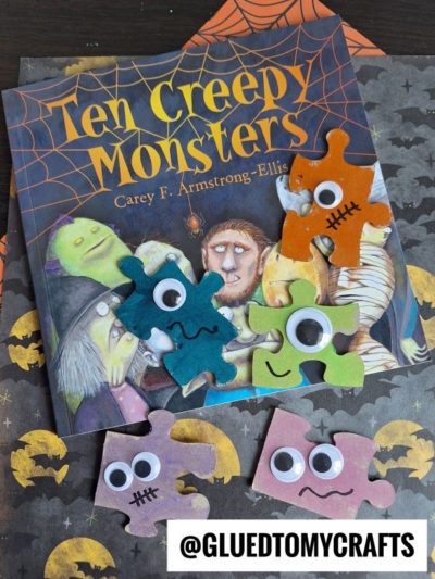 A children’s book titled Ten Creepy Monsters is surrounded by colorful puzzle piece monsters with googly eyes and stitched mouths. The background features Halloween-themed paper for a playful, spooky vibe.