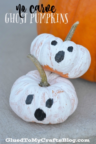 Two small white-painted pumpkins with black ghost faces are stacked together in front of an orange pumpkin. The text reads No Carve Ghost Pumpkins and GluedToMyCraftsBlog.com—perfect for creative no carve pumpkin ideas!.