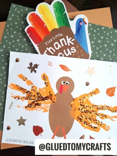 A turkey kid crafts project features a handprint turkey made with orange, brown, and yellow paint and glitter on autumn-themed paper, accompanied by a “Five Little Thank-Yous” handprint card. The handle @GLUEDTOMYCRAFTS appears at the bottom.