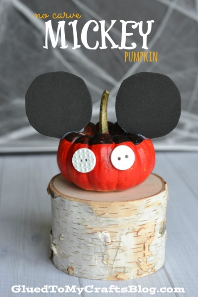 A small pumpkin painted red and black with white buttons and large black paper ears, styled to look like Mickey Mouse, sits on a cut wooden log. No Carve MICKEY Pumpkin is written above—perfect for creative no carve pumpkin ideas.
