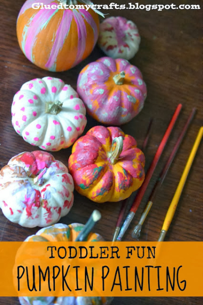 A group of small pumpkins painted with colorful designs, surrounded by paintbrushes on a wooden table. Text at the bottom reads, Toddler Fun Pumpkin Painting—perfect for creative no carve pumpkin ideas.
