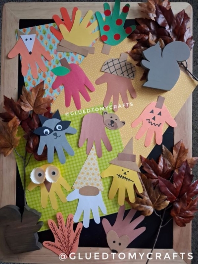 A variety of handprint cutouts decorated as animals and autumn-themed characters, surrounded by artificial leaves on a wooden frame—perfect inspiration for your next Fall Craft Ideas project.