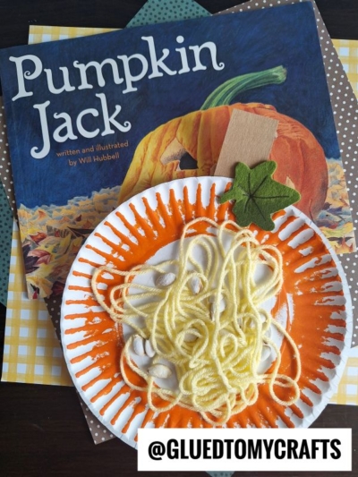 A paper plate yarn pumpkin decorated with orange paint and yellow yarn to resemble a pumpkin sits in front of the book Pumpkin Jack. A green felt leaf is attached, and @gluedtomycrafts is written at the bottom.