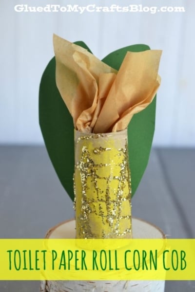 A toilet paper roll corn cob is created by painting a toilet paper roll yellow and adding gold glitter for a sparkling effect. The top is wrapped with brown tissue, while a green paper leaf placed behind completes the look, making it closely resemble an ear of corn.