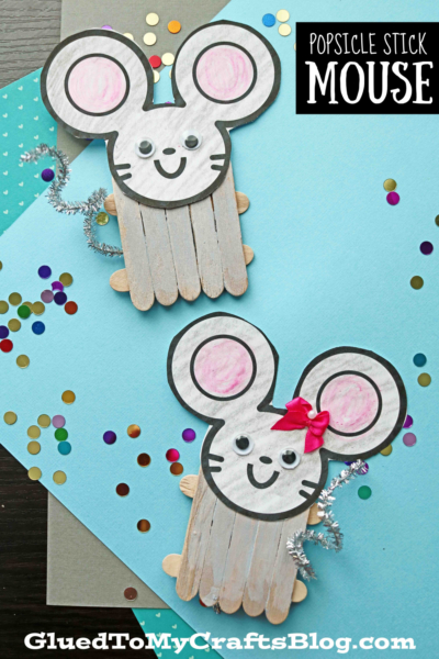Two popsicle stick mouse crafts feature paper faces, googly eyes, drawn details, and curly pipe-cleaner tails. One mouse wears a red bow. Colorful confetti adds fun to the blue background.