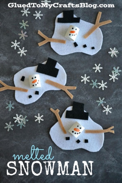 Three melted snowman crafts made with white felt, marshmallows for heads, black felt hats, orange paper noses, and stick arms, surrounded by snowflake confetti on a dark surface. This adorable melted snowman kid craft is perfect for winter activities. Text reads melted SNOWMAN.