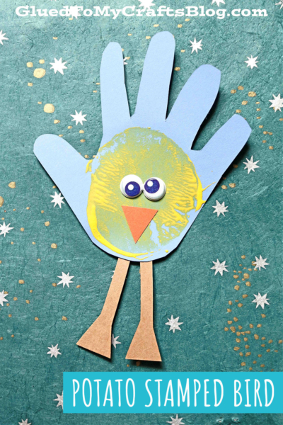 A blue Handprint Baby Birds paper cutout forms a bird with a yellow potato-stamped belly, googly eyes, an orange beak, and brown paper legs, set on a teal background with white star patterns.