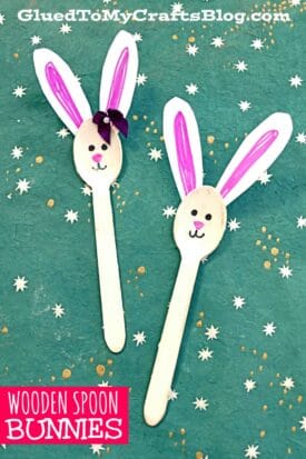 Two craft spoon bunnies with paper ears, drawn faces, and one with a purple bow are displayed on a teal, star-patterned background. Text reads WOODEN SPOON BUNNIES.