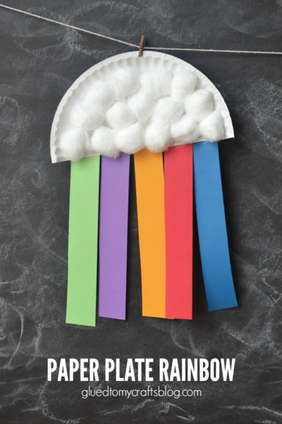 A paper plate rainbow craft features cotton ball clouds and colorful paper strips—green, purple, yellow, red, and blue—dangling like a rainbow. This cheerful rainbow cloud craft hangs on a string against a dark background.