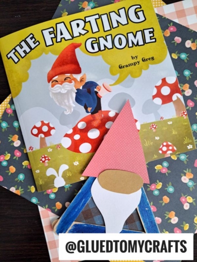 A children’s book titled “The Farting Gnome” with an illustration of a gnome and mushrooms sits beside a paper craft gnome and Popsicle Stick Gnomes. The handle @GLUEDTOMYCRAFTS appears at the bottom.