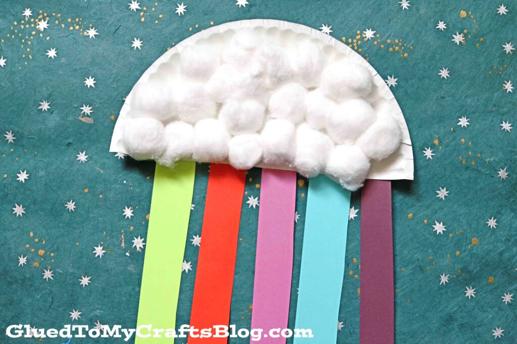 Paper plate rainbow craft with cotton ball clouds, and red, green, pink, blue, and purple streamers hanging off of it.