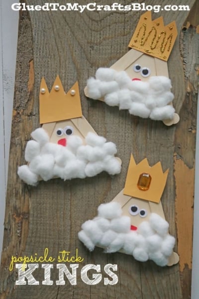 Three craft stick kings with cotton ball beards, googly eyes, crowns, and red noses sit on a wooden background.
