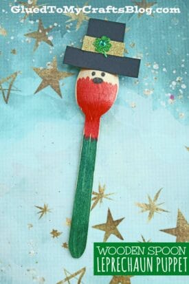 A craft spoon leprechaun puppet features a red shirt, green bottom, black hat with a green shamrock, and a simple face, all painted on a wooden spoon and set against a starry blue background.