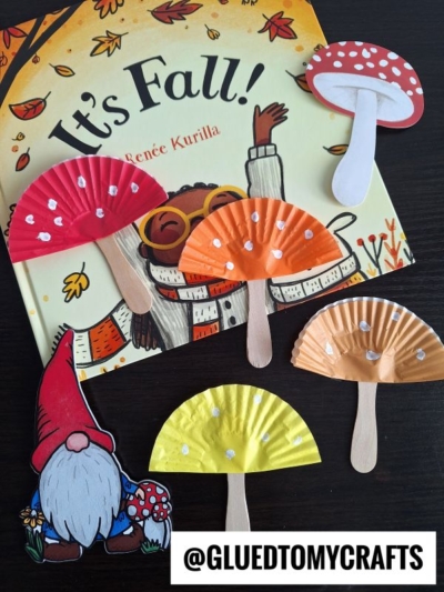 A children’s book titled It’s Fall! is surrounded by adorable mushroom kid crafts made from paper cupcake liners and craft sticks, plus a cute gnome illustration. The username @GLUEDTOMYCRAFTS appears at the bottom.