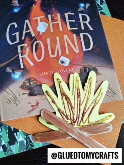A children’s book titled Gather Round by David Covell is shown, with a Handprint Popsicle Stick Campfire craft placed on top. The Instagram handle @GLUEDTOMYCRAFTS appears at the bottom.