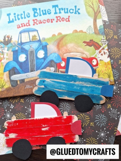 Two popsicle stick cars, one blue and one red with black paper wheels, are displayed on patterned paper in front of the children’s book Little Blue Truck and Racer Red.