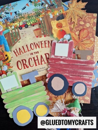 A Halloween-themed children’s book, fall leaves, and two craft stick tractors—one red, one green—are arranged on a table with a small elf doll and a “@GLUEDTOMYCRAFTS” label at the bottom.