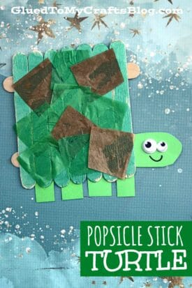 A Popsicle Stick Turtle made from green popsicle sticks with a paper head, googly eyes, a smiling face, and colorful tissue paper pieces on its back sits on a blue, starry background. Text reads: Popsicle Stick Turtle.