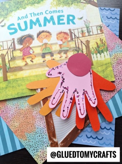 A children’s book titled And Then Comes Summer is on a table with colorful patterned paper, layered hand cutouts, and a pink glittery handprint ice cream topped with a red circle. @GLUEDTOMYCRAFTS watermark is present.