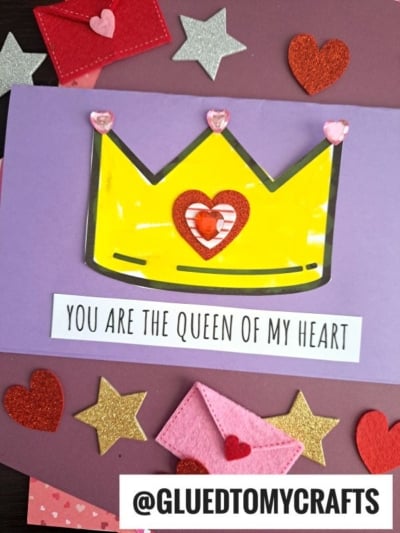 A handmade card displays a yellow crown with heart-shaped gems and a red heart, surrounded by felt stars and envelopes. The words "Queen Of My Heart" make this card a perfect way to show your love.