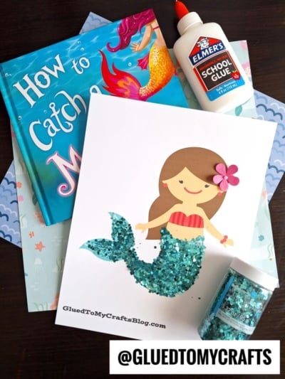 A children’s mermaid craft for kids featuring the book “How to Catch a Mermaid,” Elmer’s glue, glitter, and a finished mermaid kid craft with a sparkling glitter mermaid tail and a flower in her hair. @GLUEDTOMYCRAFTS.