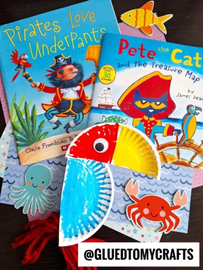 Two children’s books, “Pirates Love Underpants” and “Pete the Cat and the Treasure Map,” are displayed with colorful sea-themed crafts, including a painted paper plate parrot, a crab, and a fish. @GLUEDTOMYCRAFTS is at the bottom.
