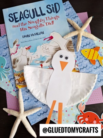 Children’s book Seagull Sid and the Naughty Things His Seagulls Did, paired with a playful paper plate seagull craft, surrounded by starfish and colorful fish-themed paper. Instagram handle @GLUEDTOMYCRAFTS at the bottom.