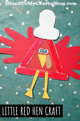 A popsicle stick little red hen craft, handmade with red wings, a triangular body, yellow legs and beak, googly eyes, and a white chef’s hat, set against a blue starry background.