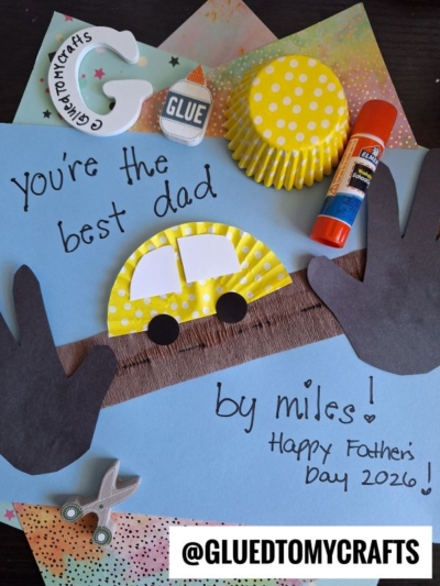 A handmade Fathers Day card with handprint cutouts, cupcake liner cars, "you’re the best dad by miles! Happy Fathers Day 2026!" written on blue paper, and craft supplies scattered around.