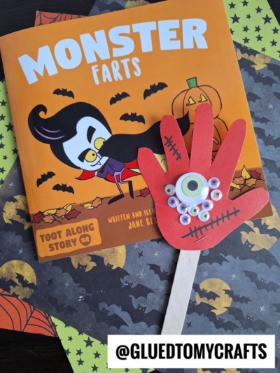 Childrens book titled Monster Farts with a cartoon vampire on the cover, surrounded by Halloween decorations, and a red hand-shaped monster craft with a googly eye and stick—perfect for fans of Monster Handprint Puppets or celebrating mommy’s little monster! @GLUEDTOMYCRAFTS text at bottom.