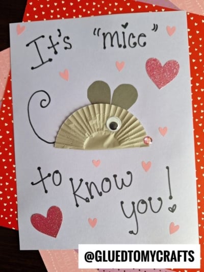 A handmade card features a cupcake liner mouse with a googly eye and paper ears, surrounded by pink and red hearts. It reads, Its mice to know you! The handle @GLUEDTOMYCRAFTS is at the bottom.