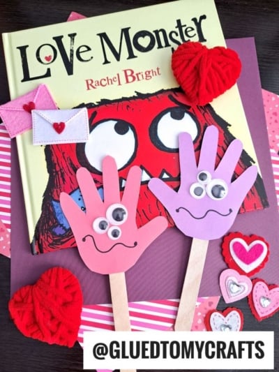 A children’s book titled Love Monster by Rachel Bright with two colorful Monster Handprint Puppets made of paper, googly eyes, and popsicle sticks, surrounded by heart-shaped decorations—perfect for mommy's little monster!.